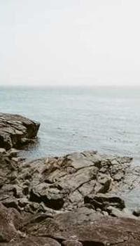 a man standing on top of a rocky beach next to the ocean